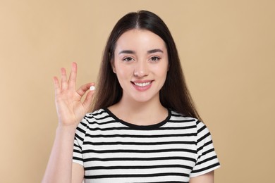 Photo of Happy woman showing pill on beige background