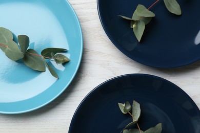 Beautiful plates with green leaves on white wooden table, flat lay