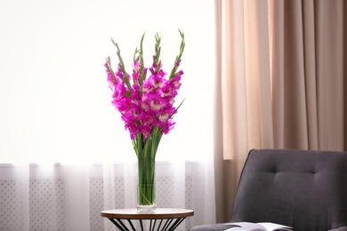 Vase with beautiful pink gladiolus flowers on wooden table in room, space for text