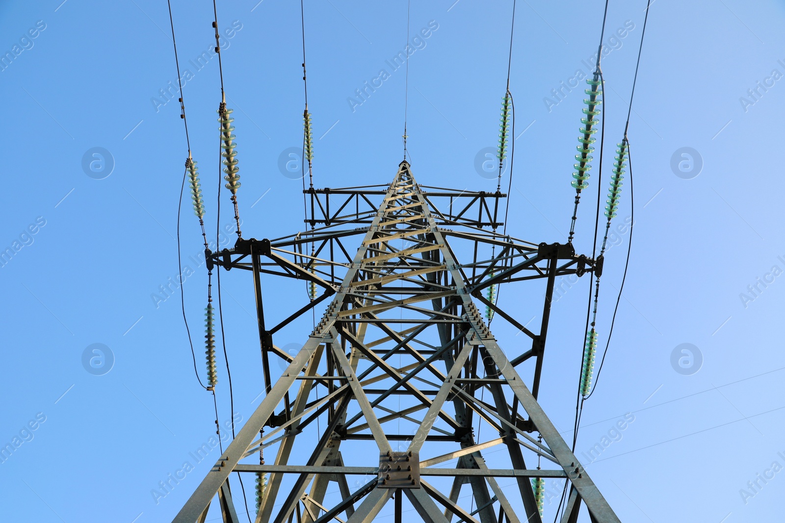 Photo of High voltage tower against blue sky on sunny day, low angle view