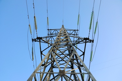 High voltage tower against blue sky on sunny day, low angle view