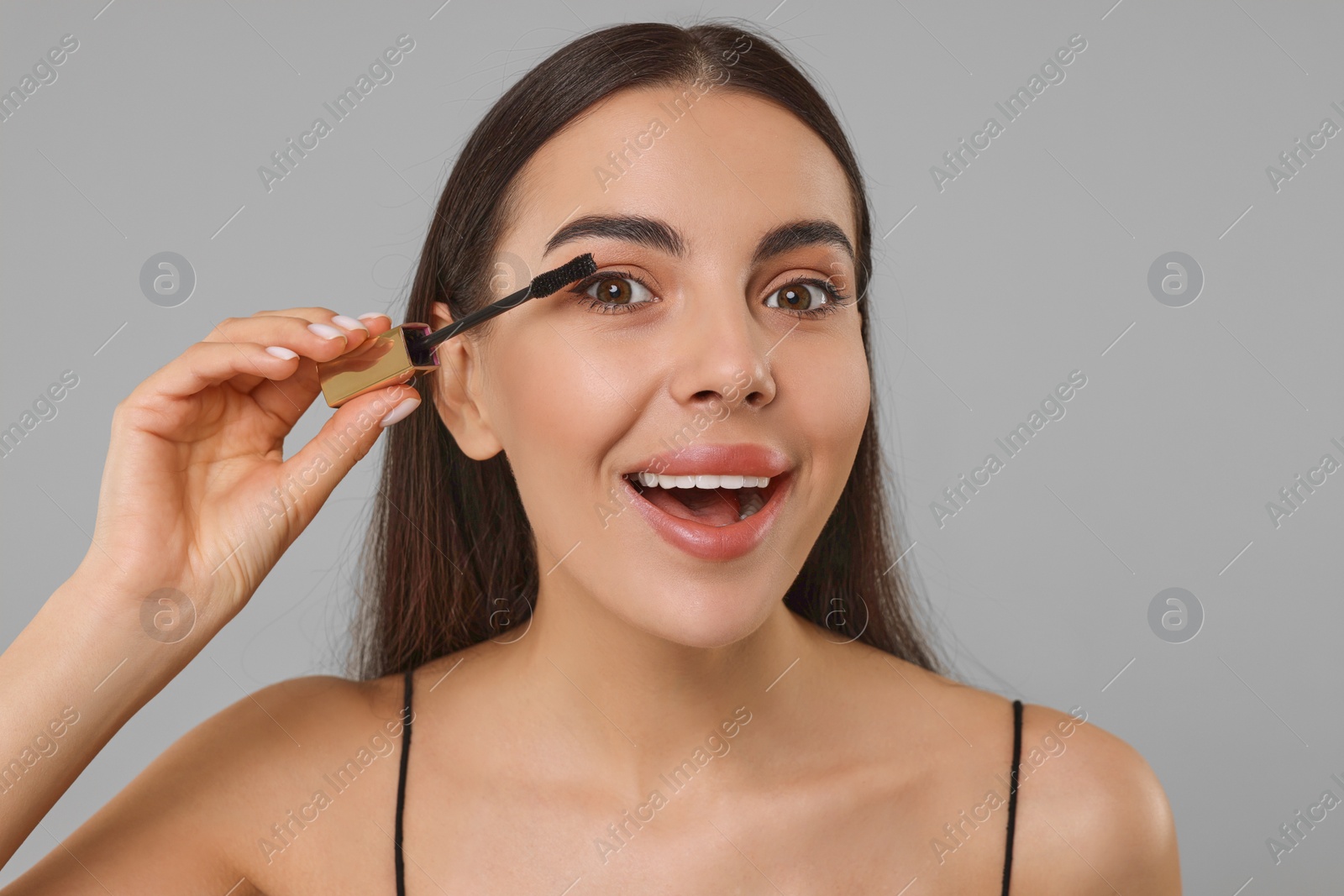 Photo of Beautiful young woman applying mascara on grey background