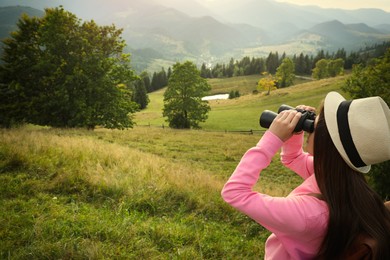 Young woman with binoculars in mountains, space for text