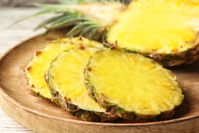 Photo of Cut fresh juicy pineapple on wooden tray, closeup