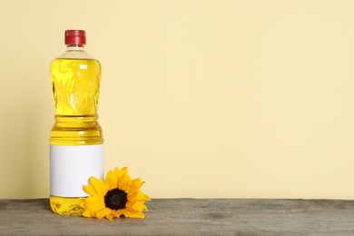 Bottle of cooking oil and sunflower on wooden table, space for text