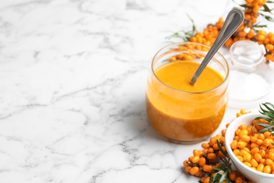 Photo of Delicious sea buckthorn jam and fresh berries on white marble table. Space for text