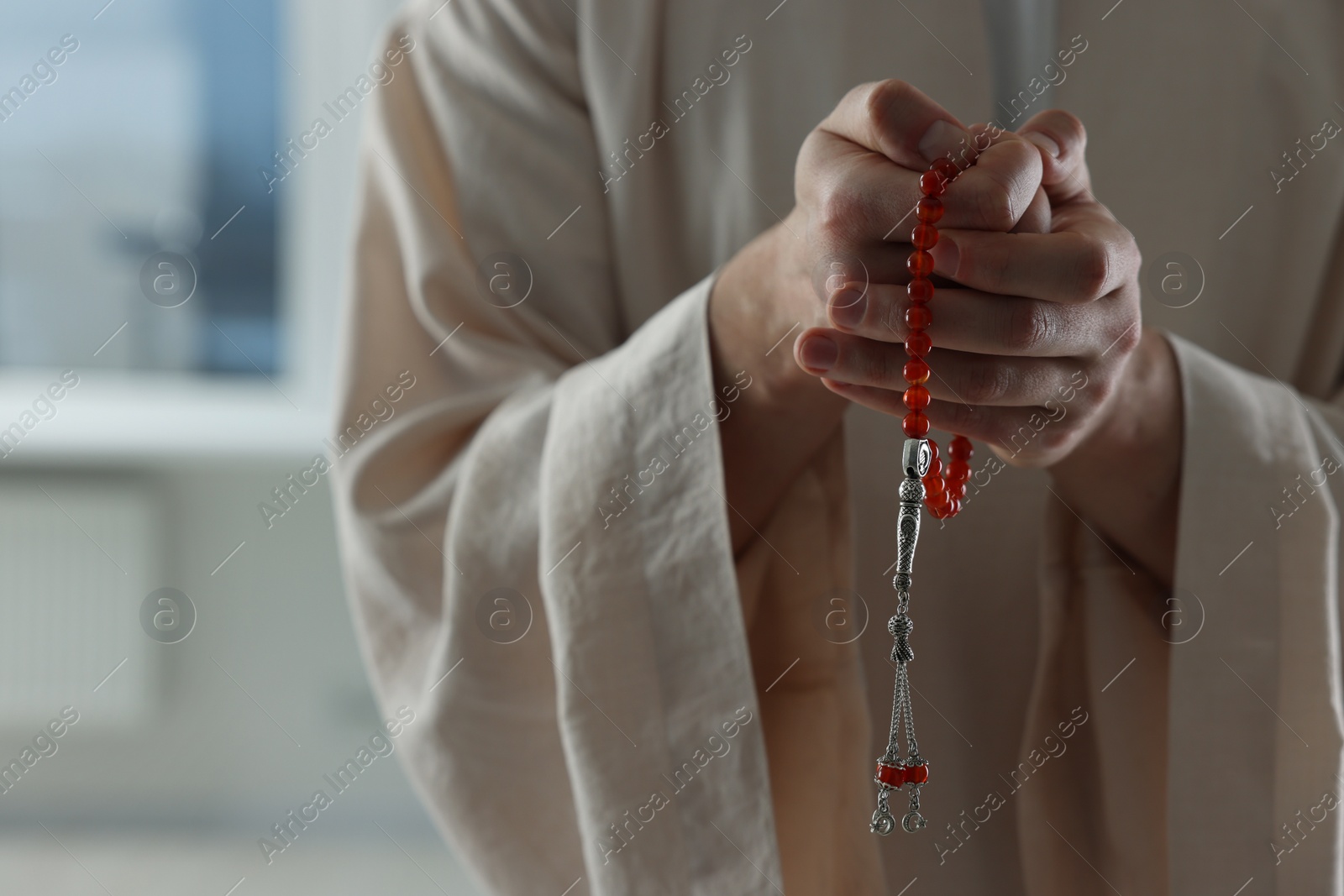 Photo of Muslim man with misbaha near window indoors, closeup. Space for text