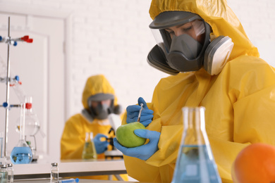 Scientist in chemical protective suit injecting apple at laboratory, space for text