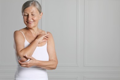 Photo of Happy woman applying body cream onto elbow near white wall. Space for text