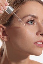 Photo of Beautiful woman applying cosmetic serum onto her face, closeup