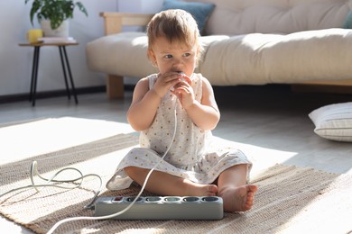 Photo of Baby girl playing with charger on floor at home. Dangerous situation