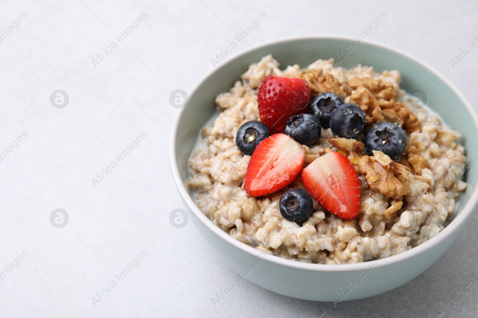 Photo of Tasty oatmeal with strawberries, blueberries and walnuts in bowl on grey table. Space for text