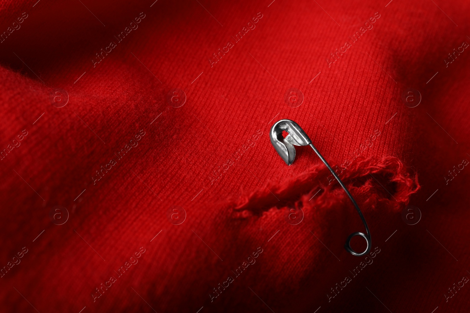 Photo of Hole on red fabric fixed with metal safety pin, closeup