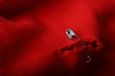 Photo of Hole on red fabric fixed with metal safety pin, closeup