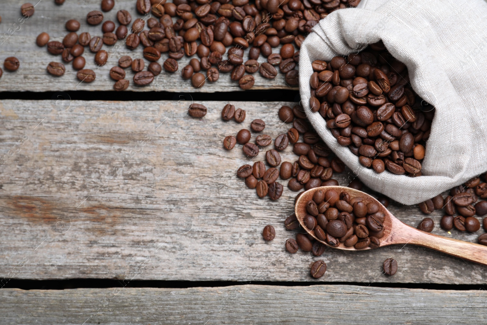 Photo of Bag and spoon with roasted coffee beans on wooden table, flat lay. Space for text