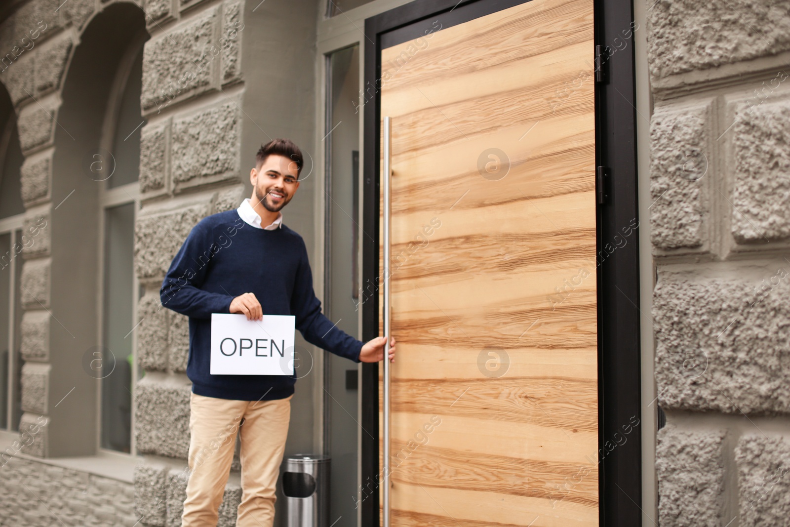 Photo of Young male business owner holding OPEN sign near his cafe. Space for text