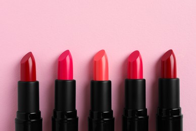 Many bright lipsticks on pink background, flat lay. Space for text