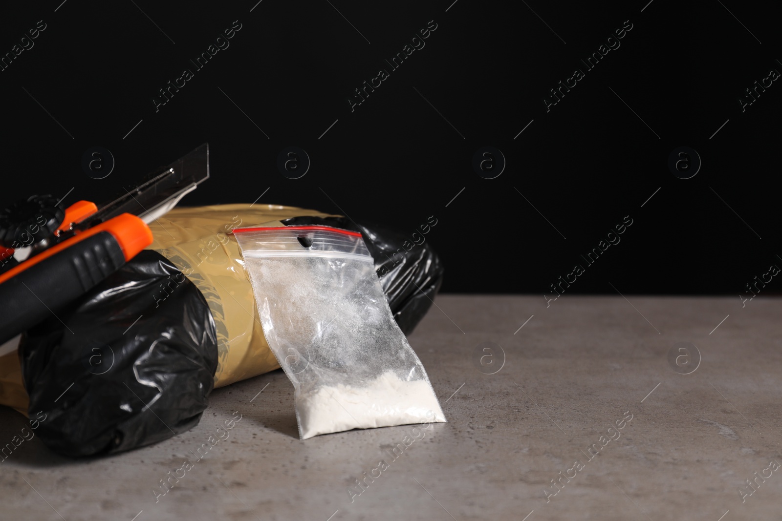 Photo of Smuggling, drug trafficking. Packages with narcotics and utility knife on grey table against black background, space for text