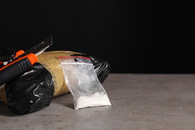 Photo of Smuggling, drug trafficking. Packages with narcotics and utility knife on grey table against black background, space for text