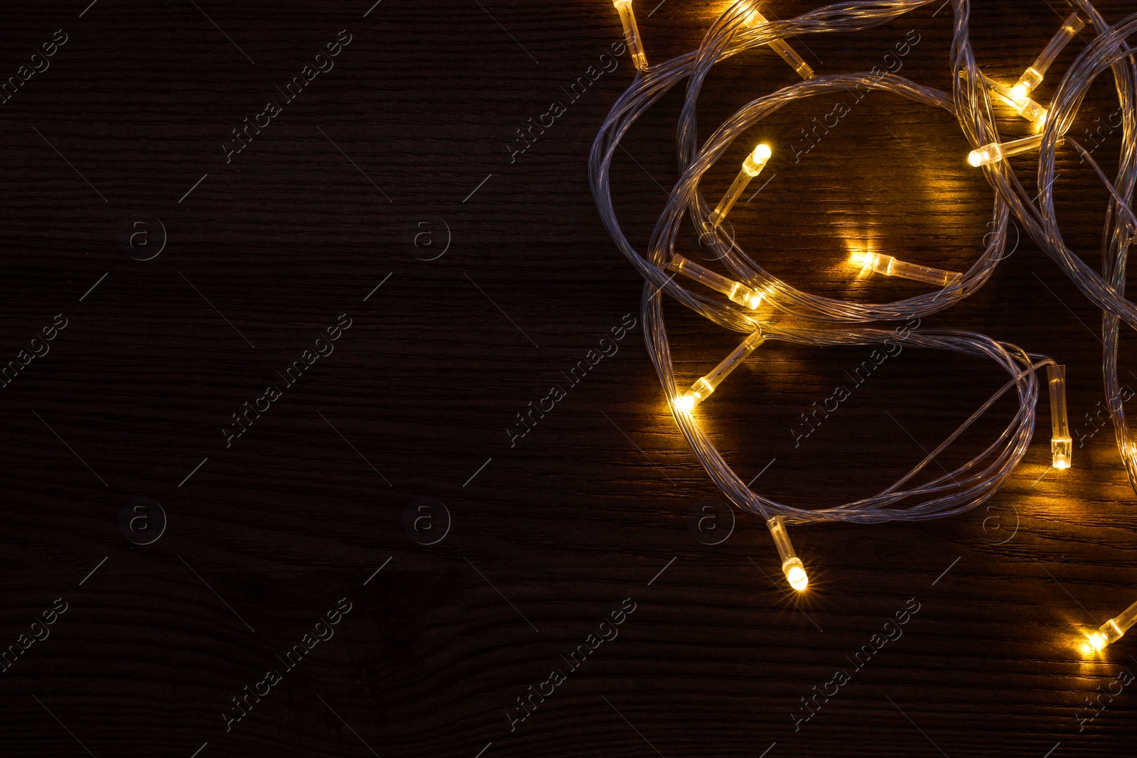 Photo of Beautiful glowing Christmas lights on wooden table, top view. Space for text