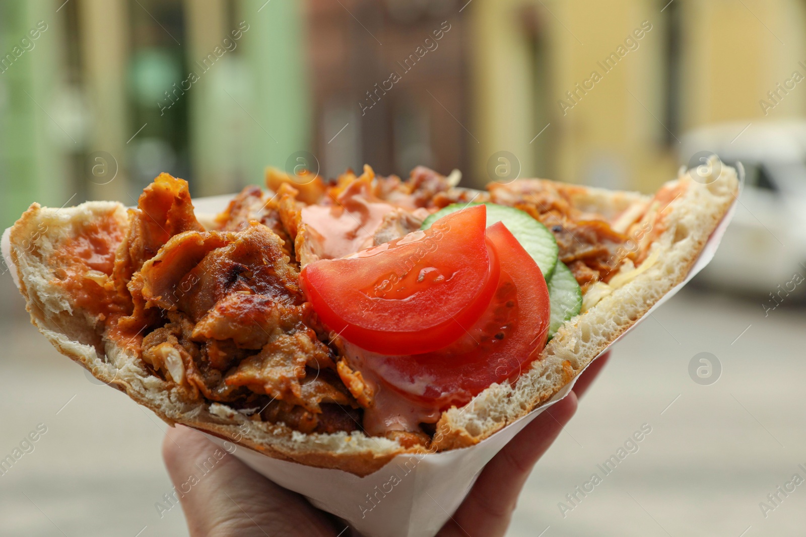 Photo of Woman holding delicious bread with roasted meat and vegetables outdoors, closeup. Street food