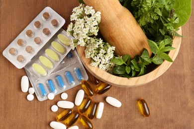 Photo of Mortar with fresh herbs and pills on wooden table, top view