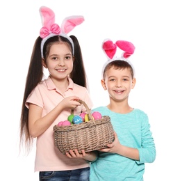 Photo of Cute children in bunny ears headbands holding basket with Easter eggs on white background