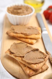 Photo of Crispy crackers with delicious meat pate and knife on wooden board, closeup
