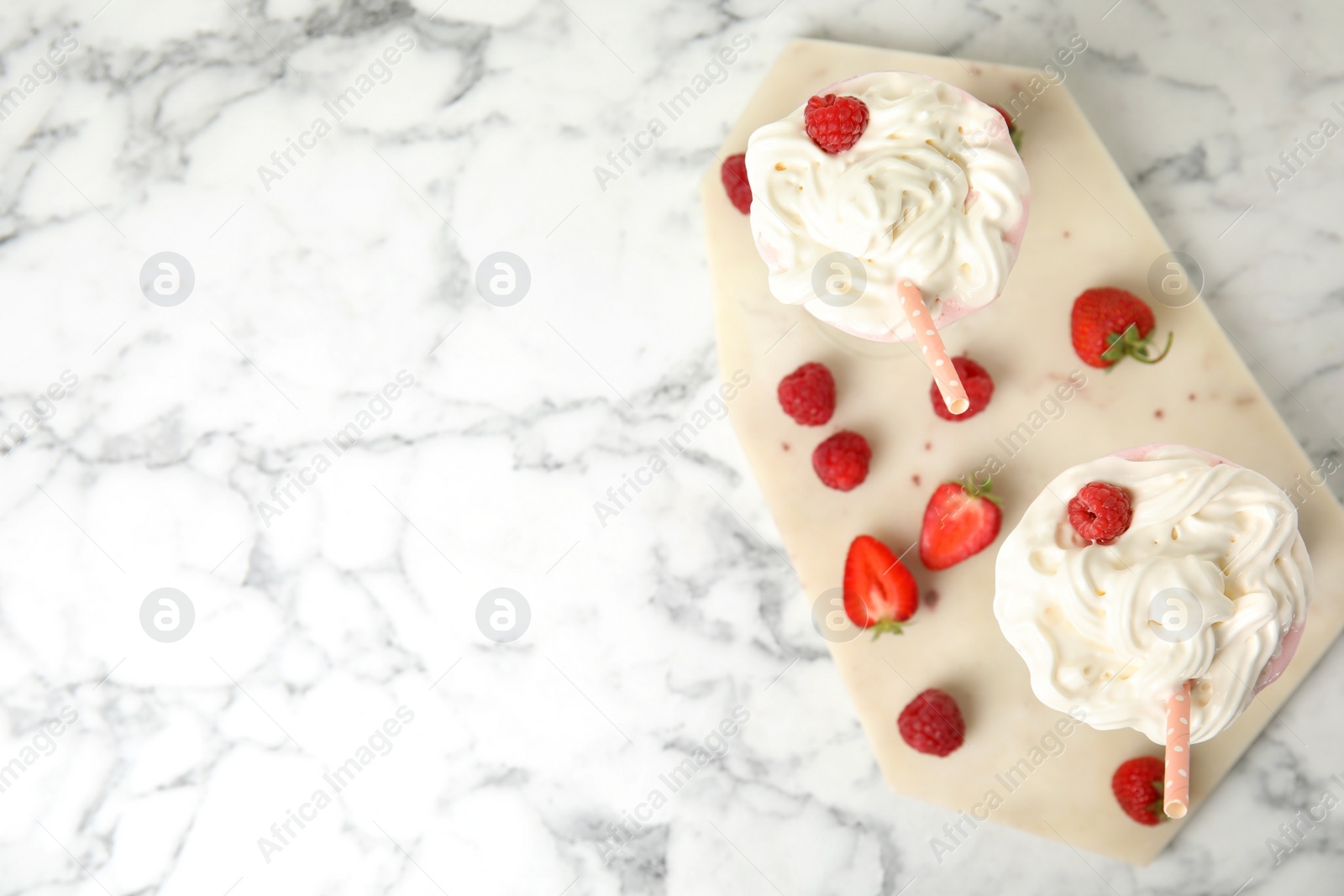 Photo of Tasty milk shake with whipped cream and fresh berries on white marble table, top view. Space for text