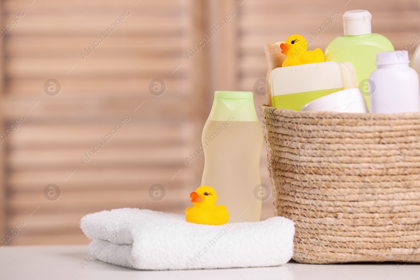 Photo of Wicker basket with baby cosmetic products, bath accessories and rubber ducks on table indoors. Space for text