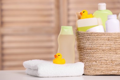 Wicker basket with baby cosmetic products, bath accessories and rubber ducks on table indoors. Space for text