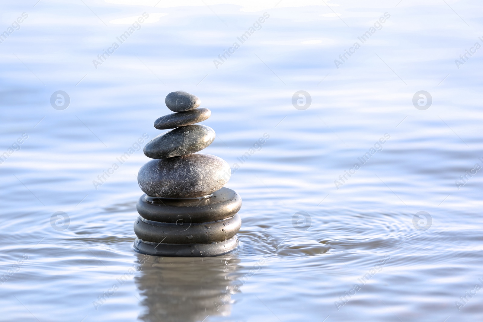 Photo of Stack of dark stones in sea water, space for text. Zen concept