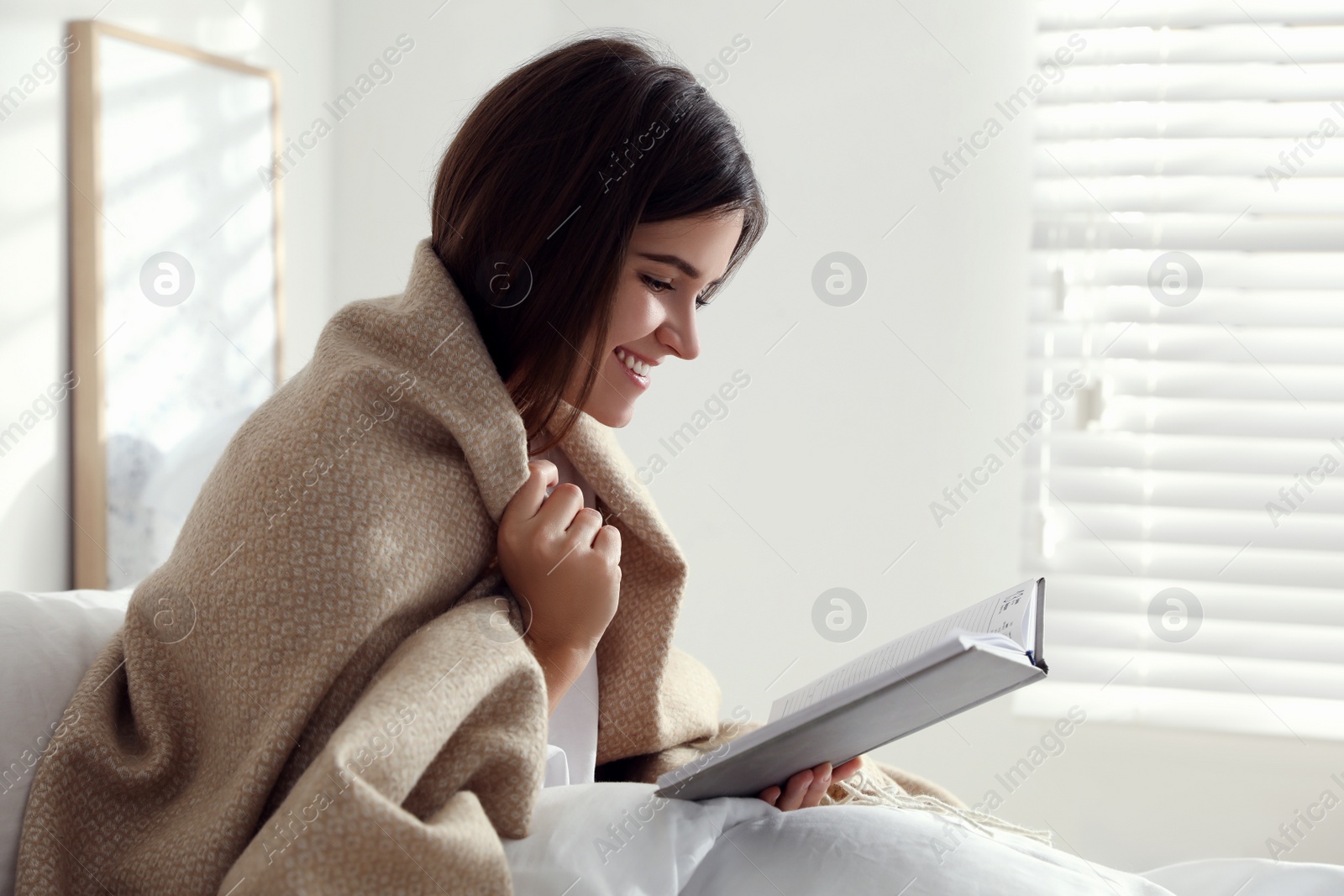 Photo of Woman with warm beige plaid reading book in bedroom