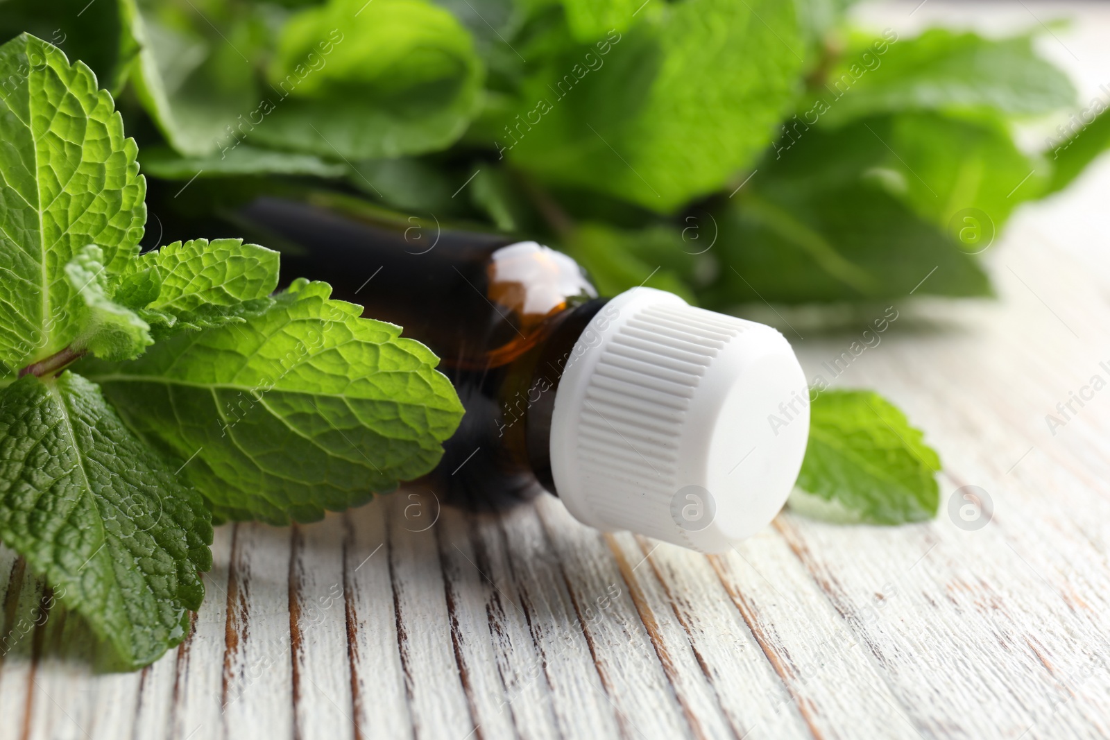 Photo of Bottle of essential oil with mint leaves on wooden table