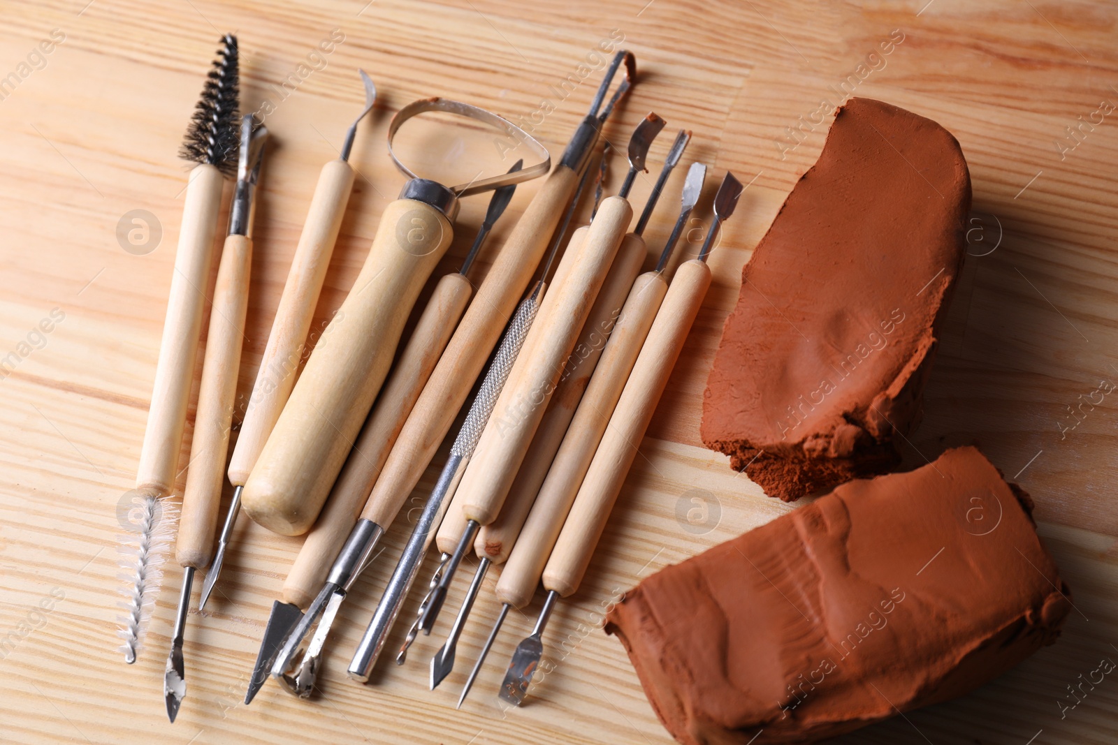 Photo of Clay and set of modeling tools on wooden table, flat lay