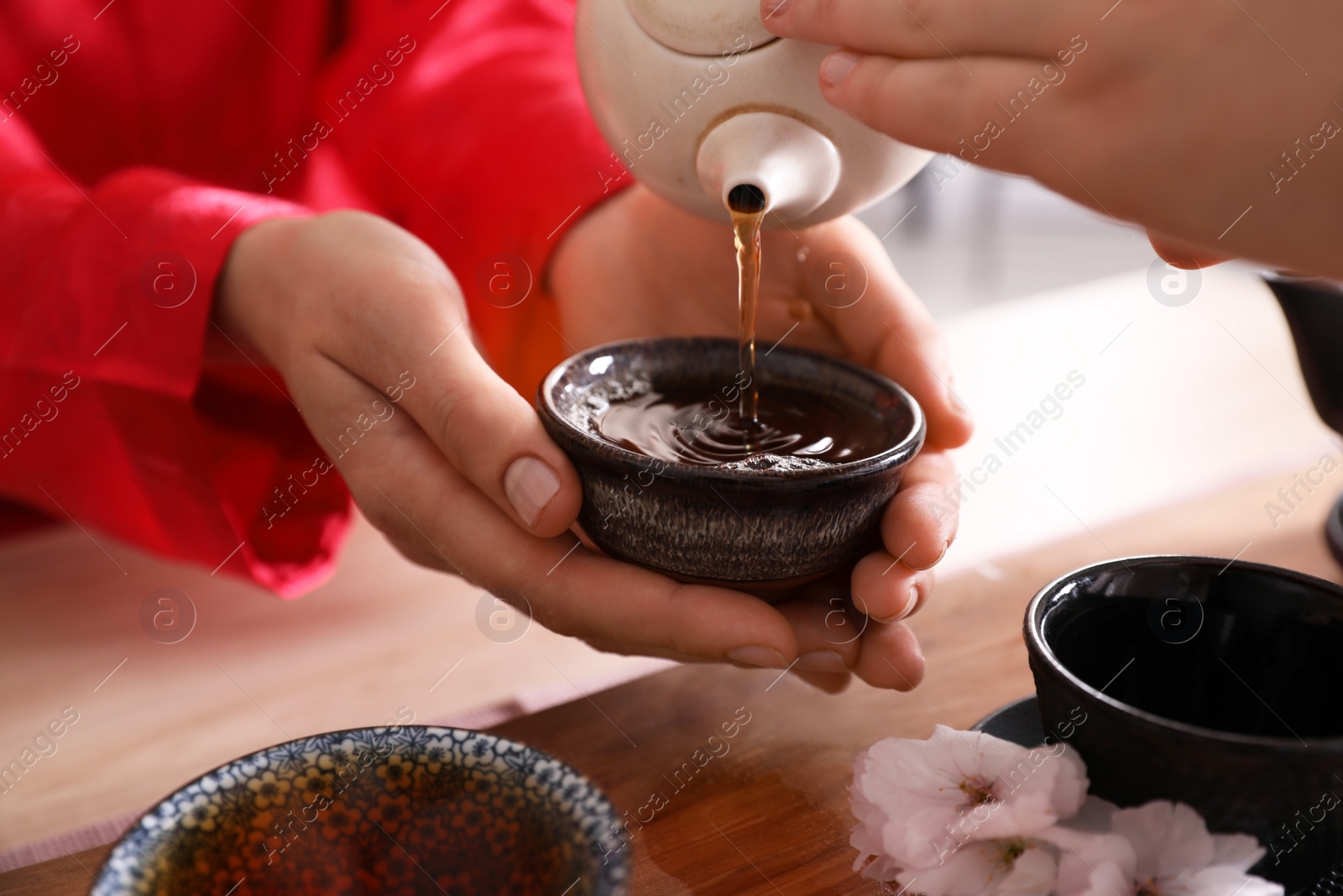 Photo of Master pouring freshly brewed tea into guest's cup during traditional ceremony at table, closeup