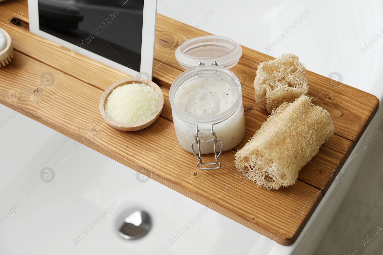 Photo of Wooden tray with tablet and spa products on bath tub in bathroom