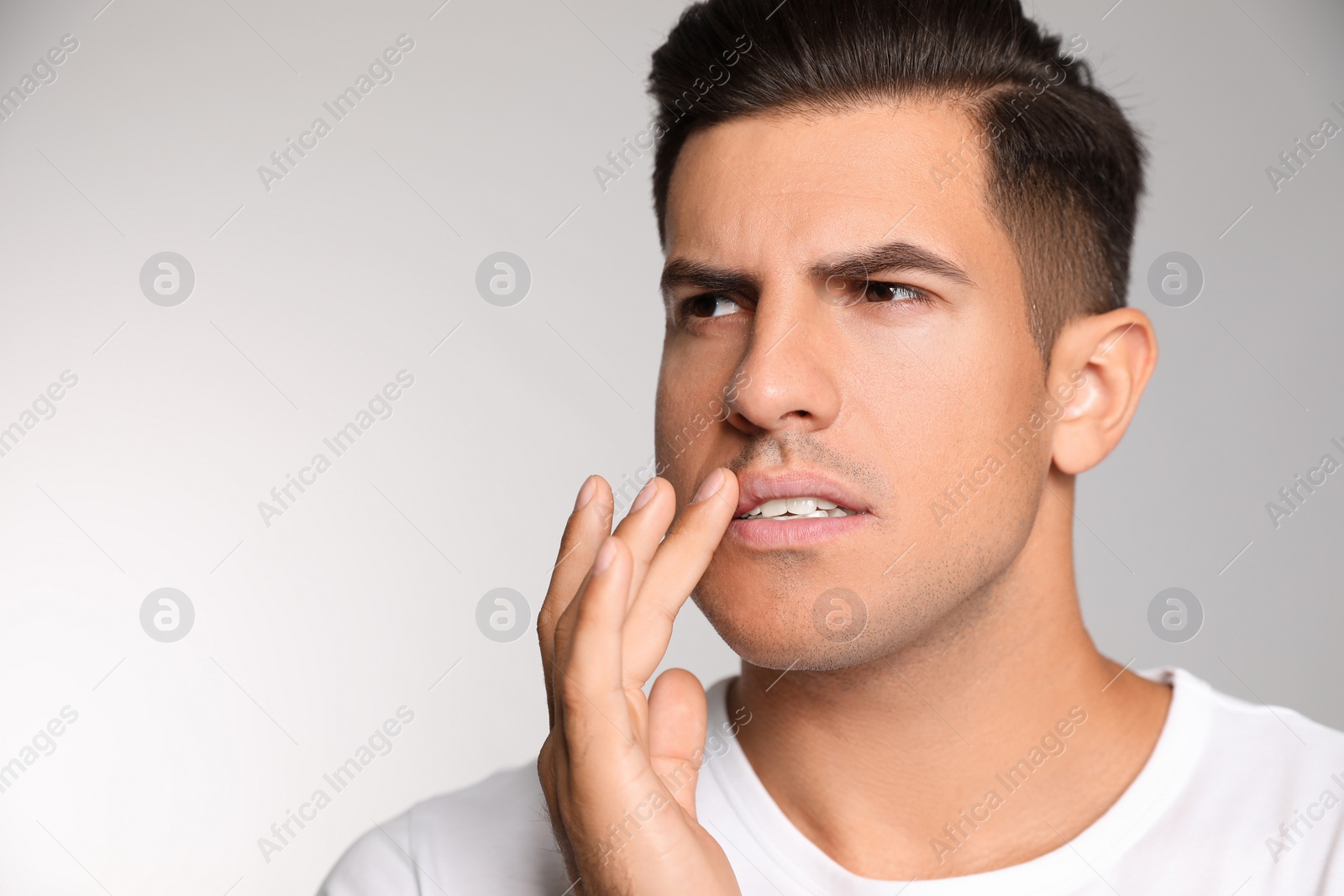 Photo of Man with herpes touching lips against light grey background. Space for text