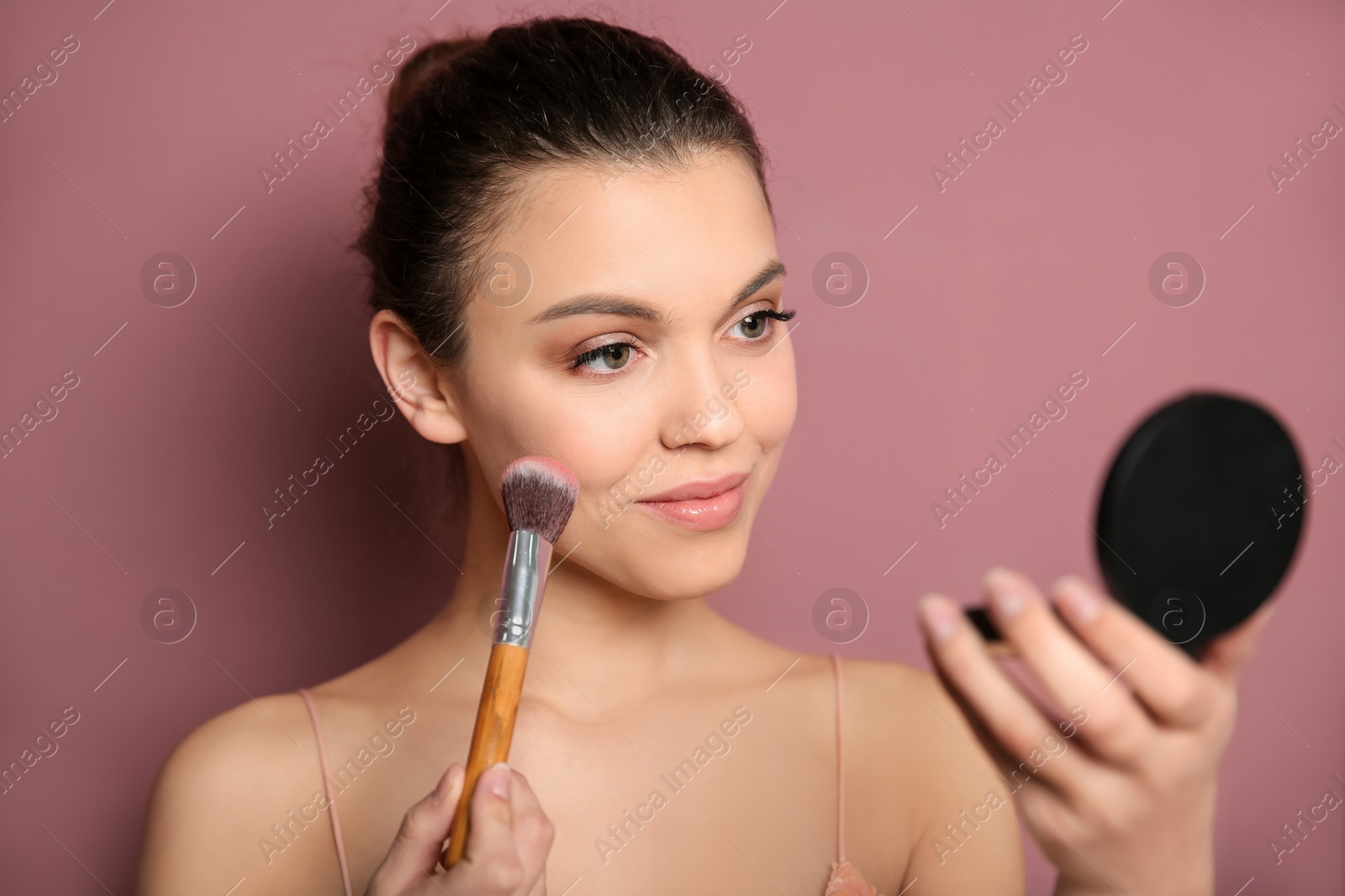 Photo of Young woman applying makeup on color background. Professional cosmetic products