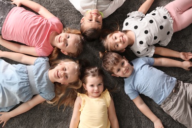Photo of Playful little children lying on carpet indoors, top view