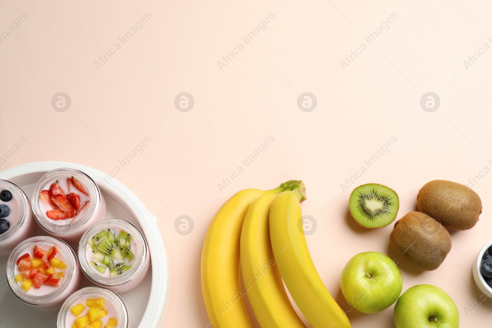 Photo of Yogurt maker with jars and different fruits on light pink background, flat lay. Space for text