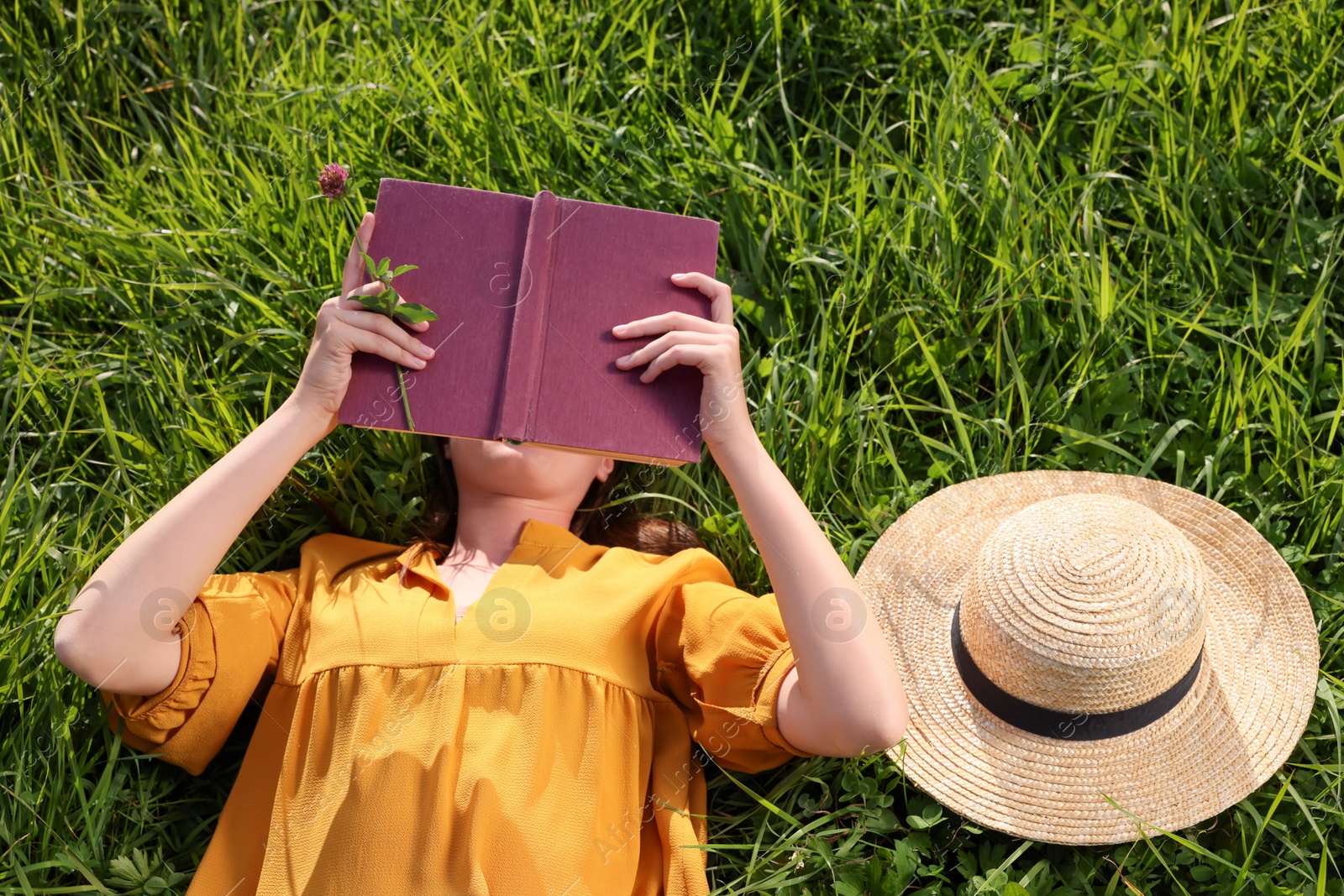 Photo of Woman reading book on green meadow, above view