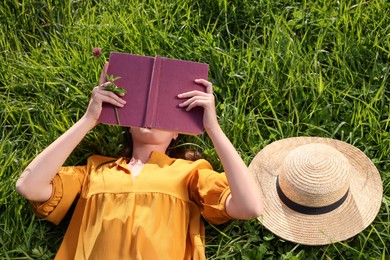 Woman reading book on green meadow, above view