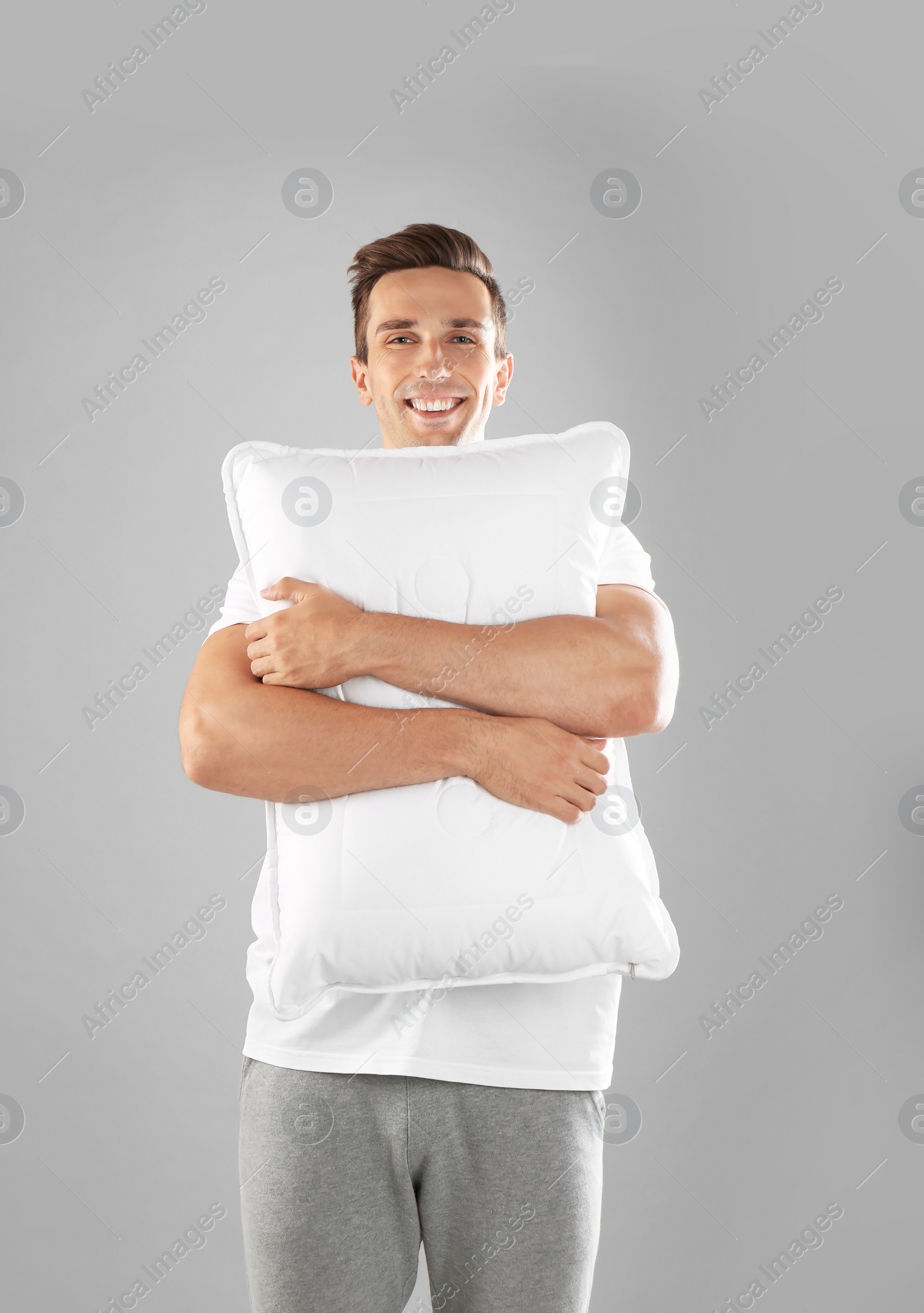 Photo of Young man in pajamas embracing pillow on gray background