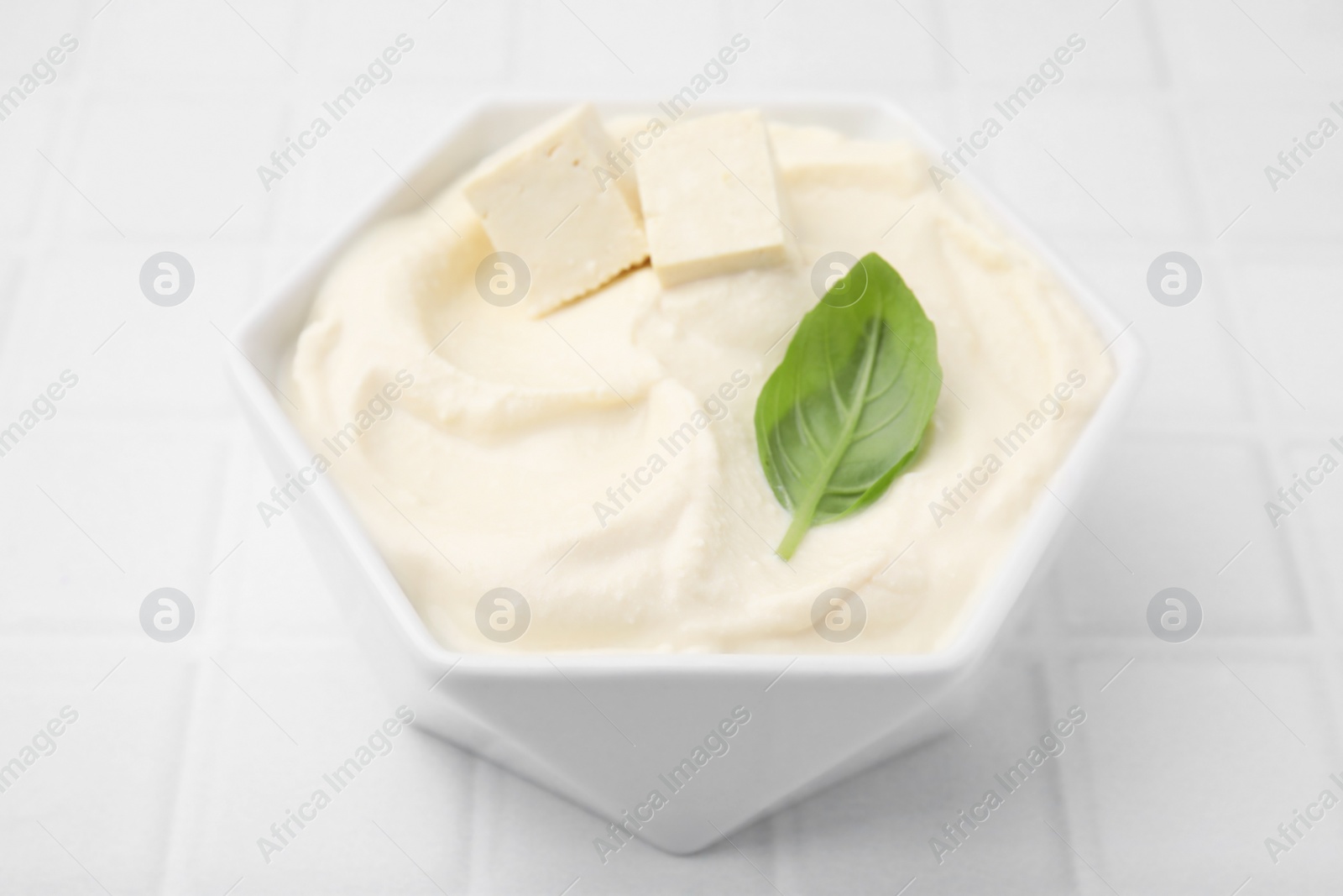 Photo of Delicious tofu sauce and basil leaf in bowl on white tiled table, closeup