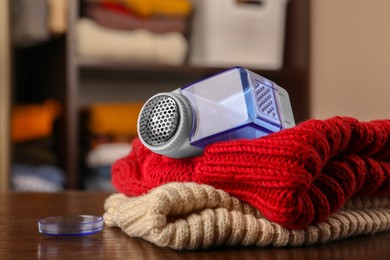 Modern fabric shaver and knitted clothes on wooden table indoors, closeup