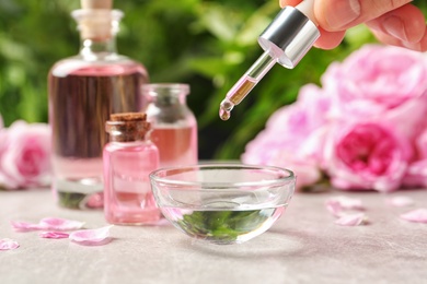 Woman dripping rose essential oil into bowl on table, closeup