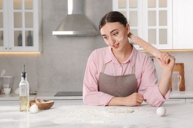 Photo of Tired woman with soiled face holding rolling pin in messy kitchen