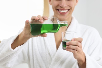 Young man using mouthwash indoors, closeup view