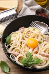 Photo of Bowl of delicious pasta Carbonara with egg yolk on wooden table, closeup